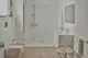 Minimalistisches Bad mit Dusche und Brausethermostat in Chrom von Ideal Standard. Helle Wände, Holzfußboden und vereinfachte Sanitäranlagen.